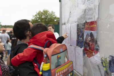 un homme tient son enfant dans les bras tout en regardant une liste de classes sous une vitre d'un panneau - Agrandir l'image 45 sur 80, fenêtre modale