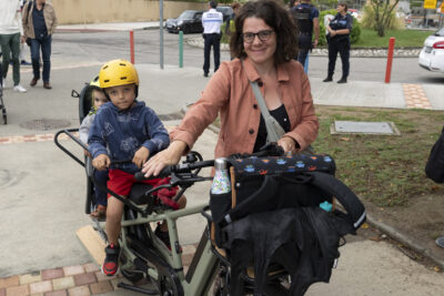 une femme marche à côté de son vélo cargo, deux enfants à l'arrière, elle sourit à l'objectif - Agrandir l'image 46 sur 80, fenêtre modale