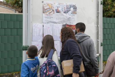 une famille devant un panneau municipal "tournefeuille informations" où sont accrochées les listes des classes, ils sont de dos, en train de lire - Agrandir l'image 40 sur 80, fenêtre modale