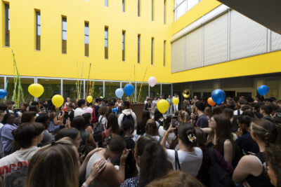 photo dans un hall jaune, avec des verrières au plafond, un groupe de musique joue et des lycéens autour écoutent, photo de derrière les lycéens et la foule - Agrandir l'image 59 sur 80, fenêtre modale