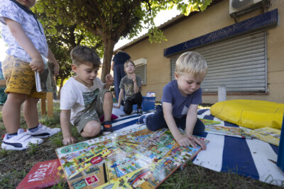 Photo paysage d'enfants par terre sur un tapis extérieur qui regardent un plateau avec plein d'illustrations colorées, derrière eux une petite fille - Agrandir l'image 6 sur 16, fenêtre modale