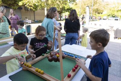 Photo paysage de trois enfants qui jouent à un jeu en bois, autour d'une table en extérieur sur une place, alors qu'il fait beau temps - Agrandir l'image 1 sur 16, fenêtre modale