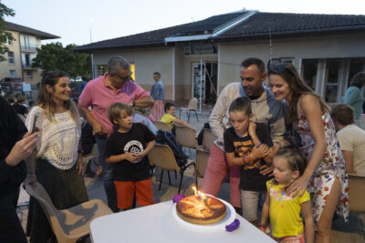 Photo d'une famille qui fête un anniversaire en soufflant les bougies d'un gâteau, alors que le soleil commence à se coucher - Agrandir l'image 10 sur 16, fenêtre modale