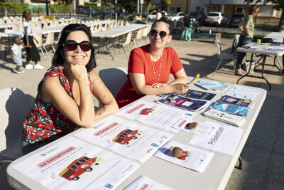 Photo de deux femmes assises à une table avec des affiches et flyers devant elles, elles sourient à l'objectif - Agrandir l'image 14 sur 16, fenêtre modale