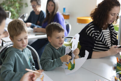 Photo de deux petits garçons qui découpent des formes de mains dans des feuilles en papier, assis à table - Agrandir l'image 12 sur 21, fenêtre modale