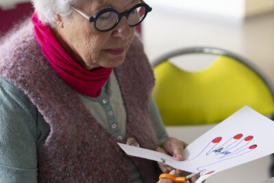 Photo d'une femme âgée qui découpe une main dans une feuille en papier - Agrandir l'image 15 sur 21, fenêtre modale