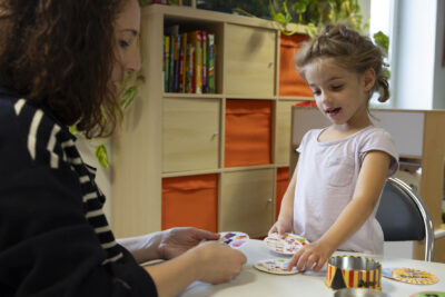 Photo d'une petite fille et d'une femme, la petite fille désigne quelque chose sur des cartes en papier ronde posées sur une table - Agrandir l'image 18 sur 21, fenêtre modale