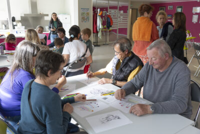 Photo de groupes de gens de tous âges assis à des tables en train de dessiner des formes de main - Agrandir l'image 9 sur 21, fenêtre modale