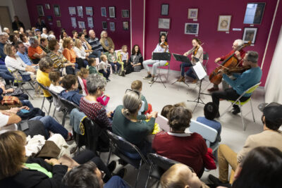 Photo d'un concert de quatre musiciens à corde, violon violoncelle et contrebasse, du monde assis sur des chaises à écouter - Agrandir l'image 10 sur 21, fenêtre modale