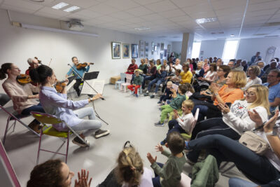 Photo du concert des quatre musiciens dans la salle remplie de monde, les gens applaudissent, au premier rang des enfants dans des petites chaises - Agrandir l'image 8 sur 21, fenêtre modale