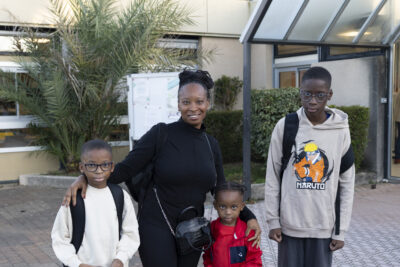 Photo d'une femme avec ses trois enfants, elle sourit, devant l'entrée de l'école - Agrandir l'image 1 sur 80, fenêtre modale