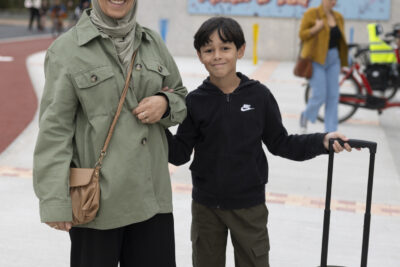 une mère et son fils sur le trottoir, souriants, il porte son sac par une poignée qui s'étend comme pour une valise - Agrandir l'image 30 sur 80, fenêtre modale