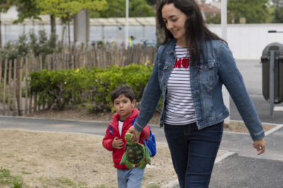 Une femme et son fils arrivent en marchant sur le trottoir, elle tient une sorte de petite peluche tortue - Agrandir l'image 29 sur 80, fenêtre modale