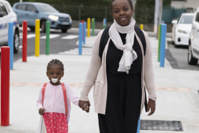 Une femme et sa fille traversent à un passage piéton récent, la petite fille porte la tétine en bouche et sa mère la tient par la main en souriant à l'objectif - Agrandir l'image 38 sur 80, fenêtre modale