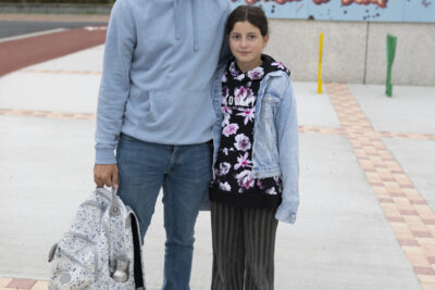 Un père et sa fille debout sur le trottoir, il tient le sac à dos de sa fille, les deux sourient - Agrandir l'image 36 sur 80, fenêtre modale