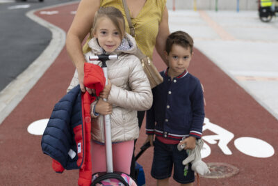 Une femme et ses deux enfants debout sur la piste cyclable rouge, le jeune fille tient son sac à dos par une poignée allongée devant elle - Agrandir l'image 33 sur 80, fenêtre modale