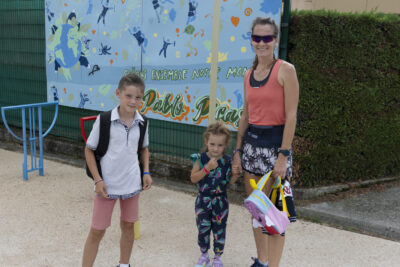 Photo d'une femme et ses deux enfants, elle tient sa fille par la main, le garçon à côté, devant la fresque bleue sur laquelle est écrit Pablo Picasso, le nom de l'école - Agrandir l'image 5 sur 80, fenêtre modale