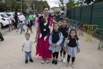 Une femme et cinq enfants, elle a un porte bébé avec un bébé, un petit garçon qu'elle tient par la main, et trois petites filles habillées de la même façon avec une robe bleue, qui sourient - Agrandir l'image 61 sur 80, fenêtre modale
