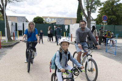 une famille arrive à vélo sur la voie cyclable devant l'école - Agrandir l'image 64 sur 80, fenêtre modale