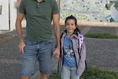 un père et sa fille, il tient sa main et ils sourient à l'objectif, devant la fresque bleue sur laquelle on peut lire "Petit train" derrière eux - Agrandir l'image 80 sur 80, fenêtre modale