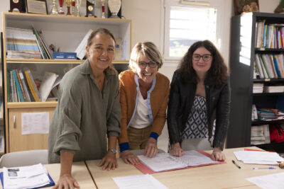 trois femmes debout, penchées au-dessus d'une table sourient à l'objectif - Agrandir l'image 77 sur 80, fenêtre modale