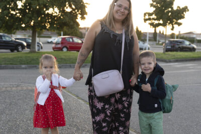une mère et ses deux enfants qu'elle tient par la main, un de chaque côté, sur le trottoir, elle sourit à l'objectif - Agrandir l'image 3 sur 80, fenêtre modale