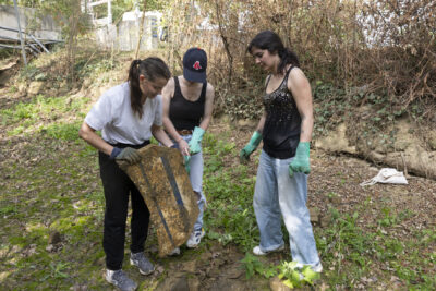 photo de trois jeunes femmes qui ramassent des déchets dans un espace vert, une tient une sorte de plaque - Agrandir l'image 9 sur 16, fenêtre modale