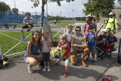 photo paysage de groupe de familles rassemblées et agenouillées devant une barrière blanche, derrière, on voit une table de ping pong, et au loin des stades de foot - Agrandir l'image 13 sur 16, fenêtre modale