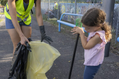 Photo portrait d'une femme et d'une petite fille, la femme porte un gilet jaune et tient un sac poubelle, la petite fille ramasse des déchets avec une pince - Agrandir l'image 2 sur 16, fenêtre modale