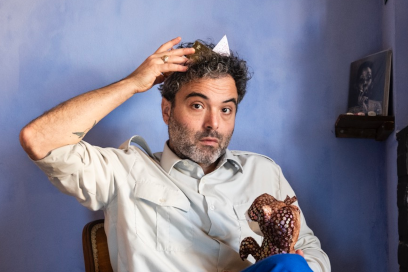 dans une chambre aux murs peints d'un bleu doux évoquant un ciel nuageux, apparaît le buste de BabX, alias David Babin, la mine surprise, assis dans un fauteuil face caméra en manches de chemises tenant de sa main droite un cône en papier figurant un petit chapeau sur sa tête aux cheveux bouclés, une peluche de serpent dans la main gauche - Agrandir l'image, fenêtre modale