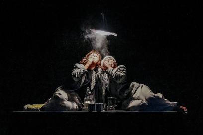 sur fond noir, allongées côte à côte dans une symétrie parfaite les deux comédiennes, en tenues de costumes d'homme des années 30, soufflent en même temps la fumée d'une cigarette dont les volutes remontent vers l'ampoule d'une suspension qui éclaire leurs visages rapprochés - Agrandir l'image, fenêtre modale