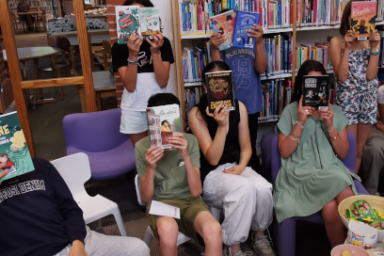 photo de groupe réalisée pendant un rendez-vous Adolector, où de jeunes lecteurs assis dans les fauteuils au milieu des rayons de la librairie cachent leur visage derrière la couverture de leur livre