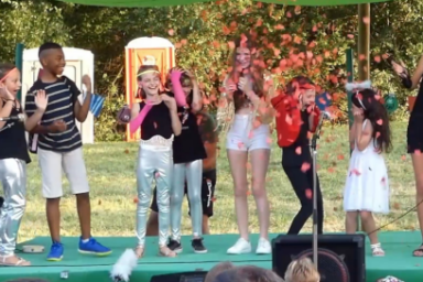 photo de jeunes debout sur une scène en plein aire qui rient face au public sous une nuée de cotillons