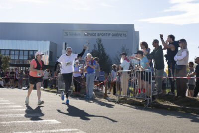 deux personnes courent sur le parking de l'espace sportif Quéfets, devant des gens qui applaudissent derrière les rubans de sécurité - Agrandir l'image 10 sur 23, fenêtre modale