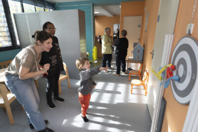 photo d'un petit garçon qui joue à un simili jeu de fléchettes, il vient de faire son lancer encouragé par deux femmes à ses côtés - Agrandir l'image 8 sur 19, fenêtre modale