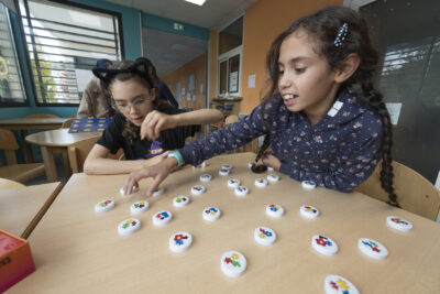 photo paysage de deux jeunes filles qui jouent à un jeu sur une table, il y a des sortes de pions ronds posés et elles les prennent - Agrandir l'image 3 sur 19, fenêtre modale