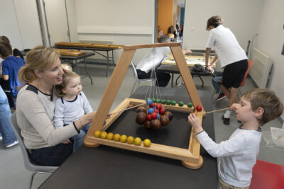 photo d'une femme qui tient une petite fille dans les bras, elles sont assises devant un jeu en bois posé sur une table, avec un petit garçon qui joue aussi - Agrandir l'image 17 sur 19, fenêtre modale
