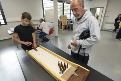 Photo d'un adulte et d'un petit garçon qui jouent à un jeu façon bowling en bois miniature avec des billes et mini quilles - Agrandir l'image 2 sur 19, fenêtre modale