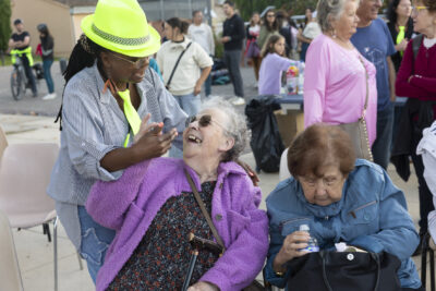 photo de trois femmes, deux plutôt âgées sont assises, une rigole avec une femme debout qui porte un chapeau jaune fluo - Agrandir l'image 13 sur 20, fenêtre modale