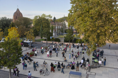 photo vue de haut du parvis de la Mairie avec des gens qui dansent, d'autres assis dans des chaises, des jeunes qui font DJ, le soleil est couchant et on voit la façade de l'église au loin - Agrandir l'image 11 sur 20, fenêtre modale