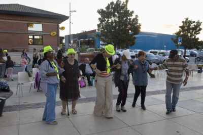 photo d'un groupe de 6 personnes qui dansent en ligne en se tenant par la main, sur le parvis de la Mairie - Agrandir l'image 19 sur 20, fenêtre modale