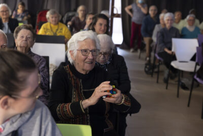 dans une salle bien remplie de personnes âgées, on voit notamment une femme faire un rubik's cube - Agrandir l'image 10 sur 20, fenêtre modale