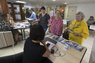Photo d'un stand avec deux femmes âgées qui viennent échanger avec la personne qui tient le stand, on voit d'autres stands à côté - Agrandir l'image 6 sur 20, fenêtre modale
