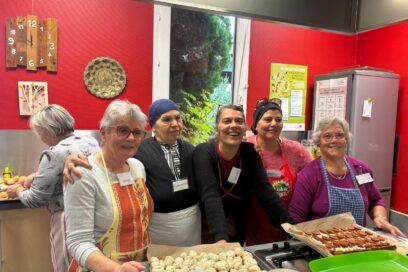 photo paysage de cinq femmes souriantes, portant chacune un tablier, debout derrière un plan de travail sur lequel on voit des préparations culinaires type apéritif - Agrandir l'image, fenêtre modale