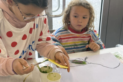 photo d'une jeune fille qui met de la peinture verte sur un outil jaune, une sorte de petite plaque - Agrandir l'image 9 sur 10, fenêtre modale