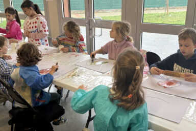photo d'une partie de la table où sont assis les enfants en train de peindre, on en voit 8 sur la photo, concentrés sur leur peinture