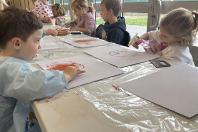 photo d'enfants occupés à peindre, au premier plan un petit garçon regarde une petite fille asperger de l'eau sur sa feuille - Agrandir l'image 2 sur 10, fenêtre modale