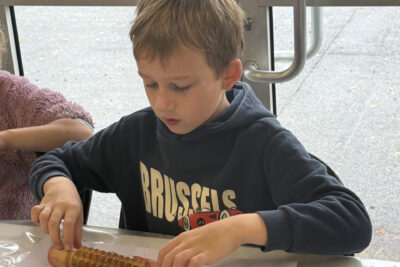photo d'un jeune garçon qui utilise un rouleau à bois avec des sortes de crans pour peindre sur sa feuille blanche avec de la peinture ocre - Agrandir l'image 5 sur 10, fenêtre modale