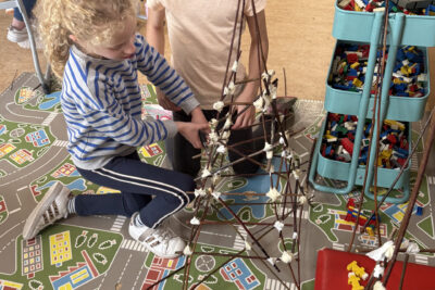 photo de deux jeunes filles par terre en train d'assembler leur lanterne magique faite de branches fines accrochées ensemble par des scotchs - Agrandir l'image 1 sur 8, fenêtre modale