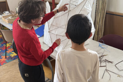 photo d'une animatrice qui montre une lanterne à un jeune garçon, la lanterne est couverte de papier blanc - Agrandir l'image 6 sur 8, fenêtre modale